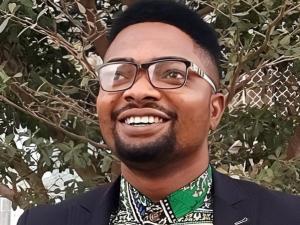 A headshot of Ayodeji outside with greenery in the background