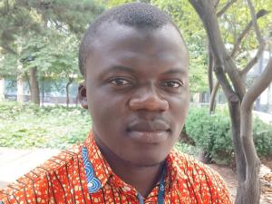 Suley is pictured outside under trees in an orange print shirt