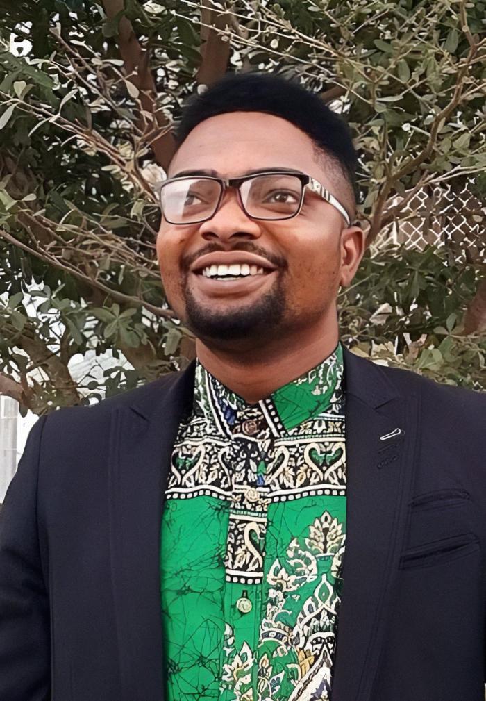 A headshot of Ayodeji outside with greenery in the background