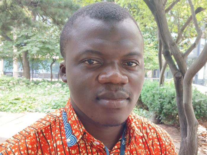 Suley is pictured outside under trees in an orange print shirt