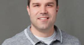 Headshot of speaker against a gray background in a relaxed polo shirt
